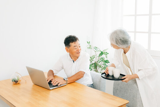 パソコンを使う高齢者男性とお茶を運ぶ女性
