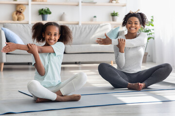 Happy black mother and daughter stretching at home