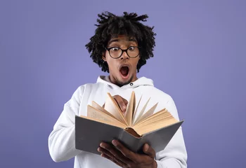 Fotobehang Black teen student looking at textbook in shock, afraid of too much homework on violet studio background © Prostock-studio