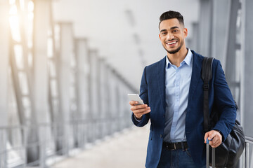 Young Middle Eastern Man With Smartphone In Hand Waiting At Airport Terminal