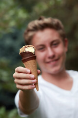 Teenage boy holding out a frozen treat ice cream cone with nuts