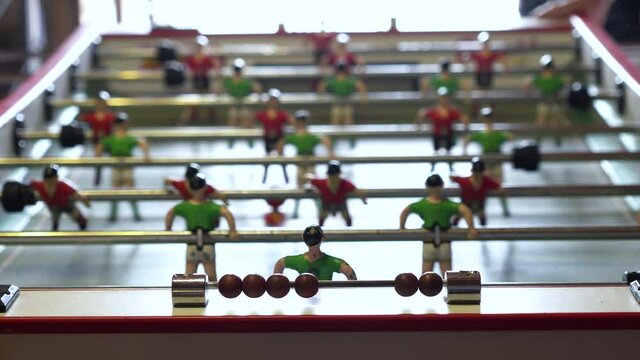 Close up shot of a table football. Hands of people playing futbolin. Small football game with green and red iron players while the table is shaking. Typical spanish soccer game.