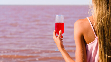 A glass with a pink cocktail in the hand of a girl on the background of a pink lake. The concept is romantic. Close-up. selective focus on wine glass.