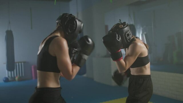 Slow motion, combat sparring of two woman fighters wearing protective helmets, training in the boxing gym, females train defence and series of punches on a battle.