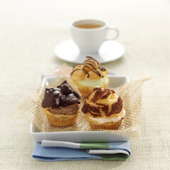 Set of three stuffed Cream Puffs, Profiterole, Bignè, or Bocconcino with a tea cup on tablecloth background. Selective focus.