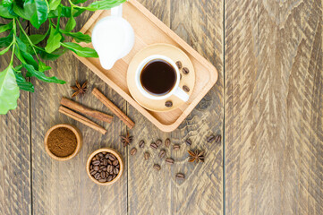 a cup of aromatic coffee and a milkman with milk on a tray. morning breakfast. green arabica coffee leaves on a wooden background.
