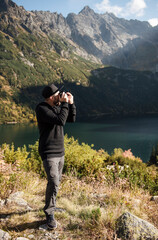 Naklejka premium Young man photographer taking photographs with digital camera in a mountains.