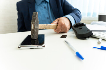 embittered businessman hits a smartphone with a hammer in workplace. Unsuccessful business...