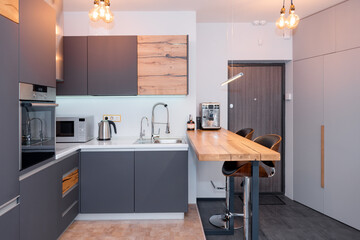 Modern kitchen interior with lights on. Brown wooden table and bar stools, coffee machine....