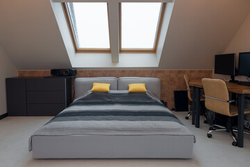 King-size bed with yellow and grey bedding in modern bedroom. Stylish room interior with comfortable bed and workplace.