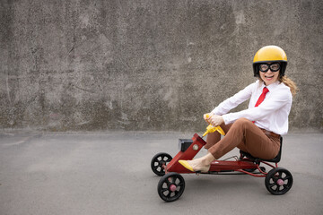 Funny businesswoman driving retro pedal car outdoor