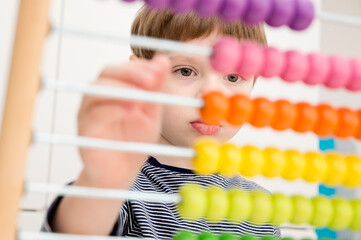 A cute kid is playing with an abacus at home. A smart child learns to count. Wooden figure...