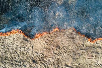Aerial view of grassland field burning with red fire during dry season. Natural disaster and climate change concept