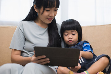 Fototapeta premium Happy asian family mother and son using tablet for education. Little boy watching funny social media. Mom with kid using tablet video call to father.