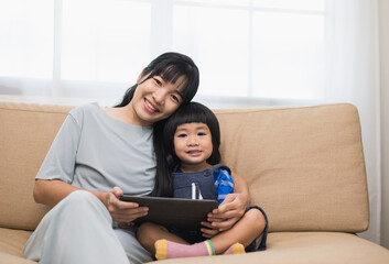 Fototapeta premium Happy asian family mother and son using tablet for education. Little boy watching funny social media. Mom with kid using tablet video call to father.