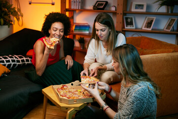 Happy multicultural female friends having party at home and eating pizza.