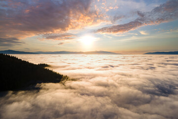 Obraz premium Aerial view of yellow sunset over white puffy clouds with distant mountains on horizon.