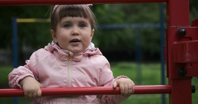 Cute baby girl having fun climbing monkey bars at park