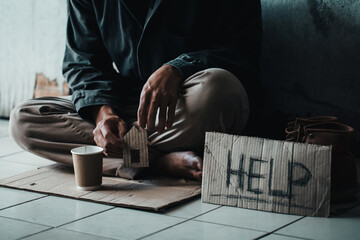 Fototapeta na wymiar Poor tired depressed hungry homeless man holding a cardboard house. with 