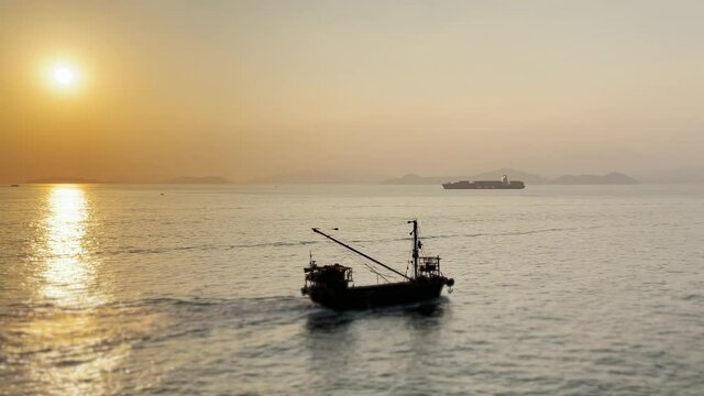 Static shot of Fishing Boat Crossing from left to right as the Sun sets. Cargo ship in the background, South China Sea