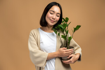 Portrait of delighted female person holding flower plant in pot while posing with closed eyes