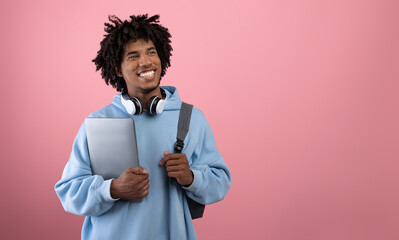 Positive African American teen student with backpack, tablet pc and headphones studying online on...