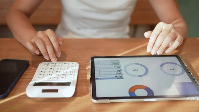 slow motion accounting woman hand pressing on calculator and check data on tablet for summarize about monthly profit of business for senior accountant job working concept