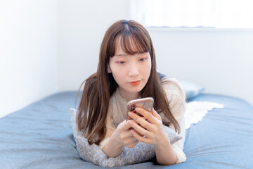 ベッドでうつ伏せでスマホを眺める女性