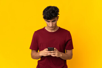 Young Argentinian man isolated on yellow background using mobile phone