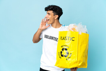 Young Argentinian man holding a bag full of plastic shouting with mouth wide open to the side