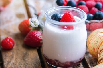 yogurt with wild berries and measuring tape. diet and eating concept