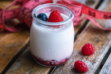 yogurt with wild berries and measuring tape. diet and eating concept