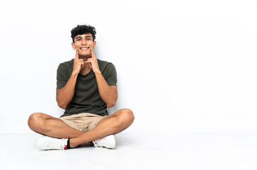 Obraz premium Young Argentinian man sitting on the floor smiling with a happy and pleasant expression