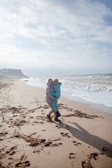 Happy family, mother and teenage daughter walking in the beach and have fun in wind weather in cold day