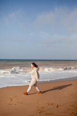 Beautiful woman wearing casual clothes, biege leggings, walking in windy sprin cold weather in the beach against the ocean.  Overweight woman have fun and enjoy the mood of view