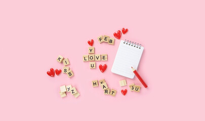 word phrase made of wooden letters, red hearts, notebook and pencil on pink background. crossword, love words. symbol of love, Romance. Valentine's Day, 14 February concept. top view