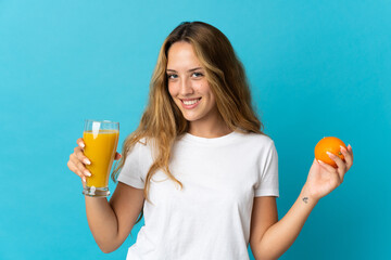 Young blonde woman isolated on blue background holding an orange and an orange juice