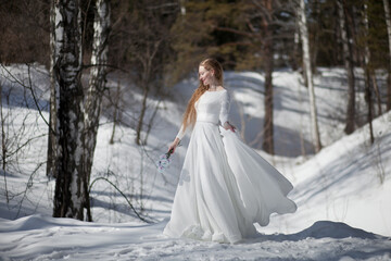 Fototapeta na wymiar blonde with long hair, a girl in a long white dress walks in the winter forest, the snow queen, the bride with a bouquet of dianthus