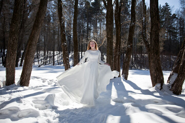blonde with long hair, a girl in a long white dress walks in the winter forest, the snow queen, the bride with a bouquet of dianthus
