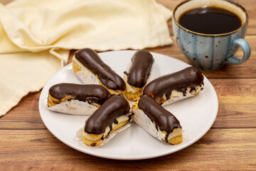 Tasty eclairs and cup of coffee on wooden table. Traditional french dessert. Pastry products. Close up