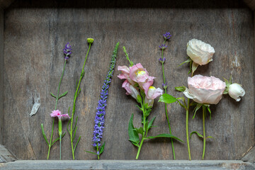 Schöne Blüten in rose und violett liegen aufgereiht in einer alten Holzkiste