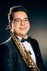 Fototapeta premium Young Japanese Saxophone Player Posing With Soprano Straight Saxophone.Musician with Brass Musical Instrument. Close-up Portrait. Black Background. High quality photo