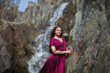 a brunette with long hair walks against the backdrop of a waterfall, a waterfall in the mountains, a photo session in a fabulous style