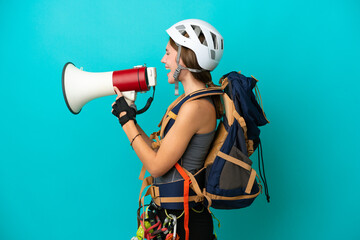 Young English rock climber woman isolated on blue background shouting through a megaphone