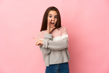 Fototapeta premium Little girl isolated on pink background pointing to the side to present a product and whispering something
