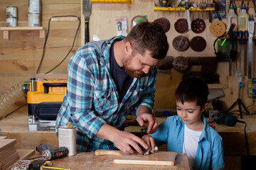 Father carpenter and son boy work in the workshop. Master dad teaches his son carpentry. Continuity of generations. Small business.