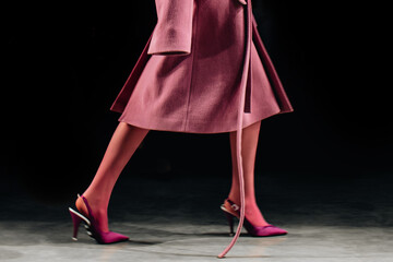Cropped female figure dressed in classic long pink fancy coat and high heels walking the runway at...