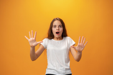 Scared young teen girl showing stop gesture against yellow background