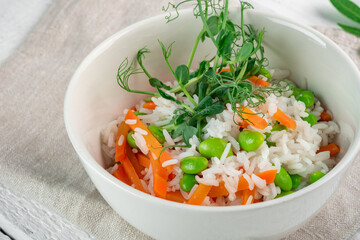 Vegan dish rice with vegetables in a white bowl on a wooden table. Steamed basmati rice with carrots, beans and pea sprouts, close up