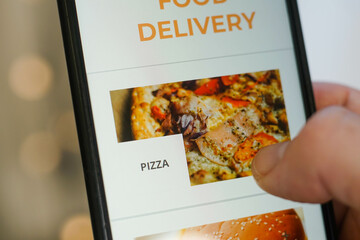 Close up of male hands using smartphone with app delivery food on screen. Young man choosing pizza.